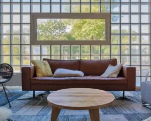 Moderne loungehoek in kantoorruimte aan de Overschiestraat 65 in Amsterdam met een bruine leren bank, ronde houten tafel en glazen bouwstenen muur.