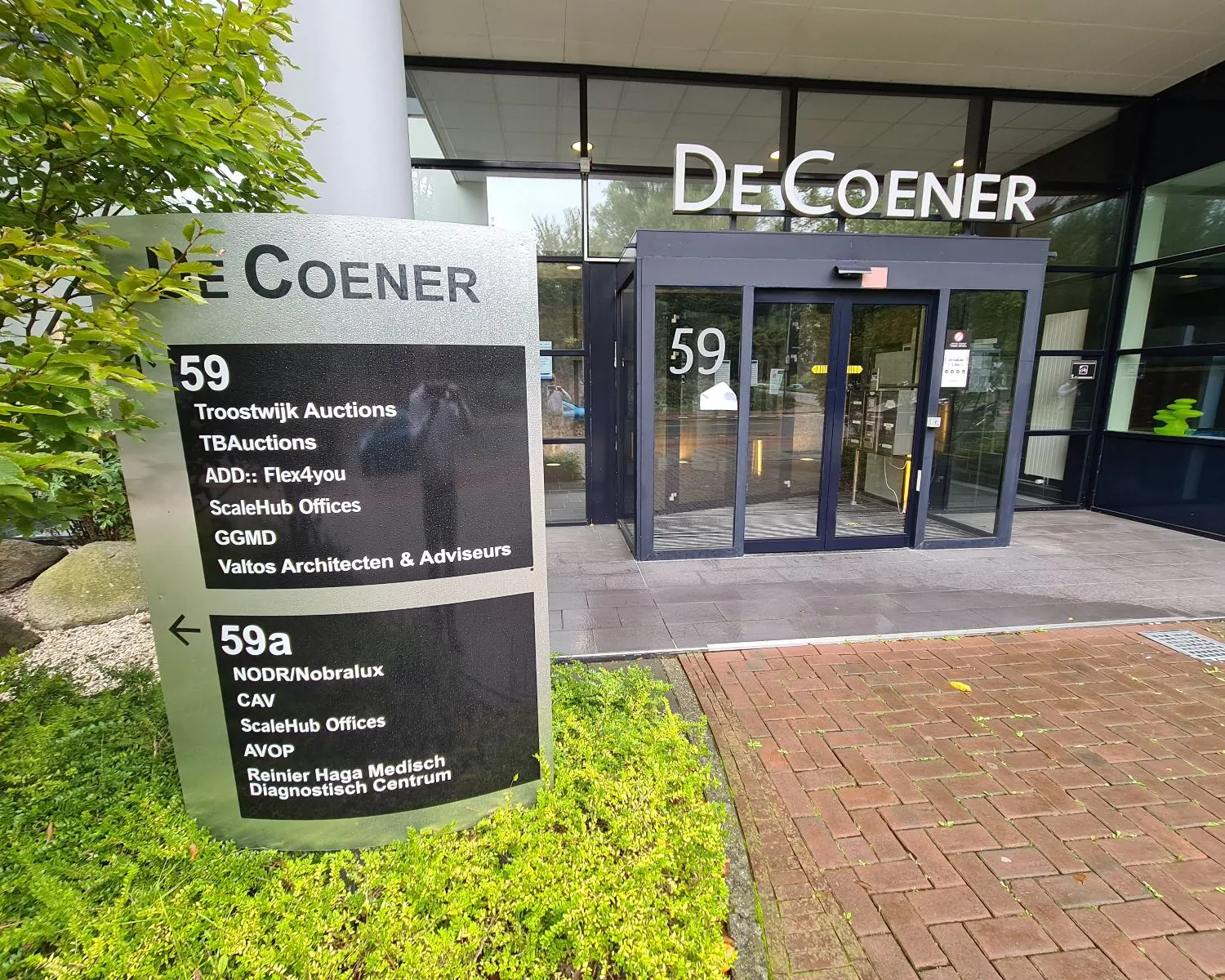 Ingang van kantoorpand De Coener aan de Overschiestraat 59 in Amsterdam met bedrijvenbord bij de entree.