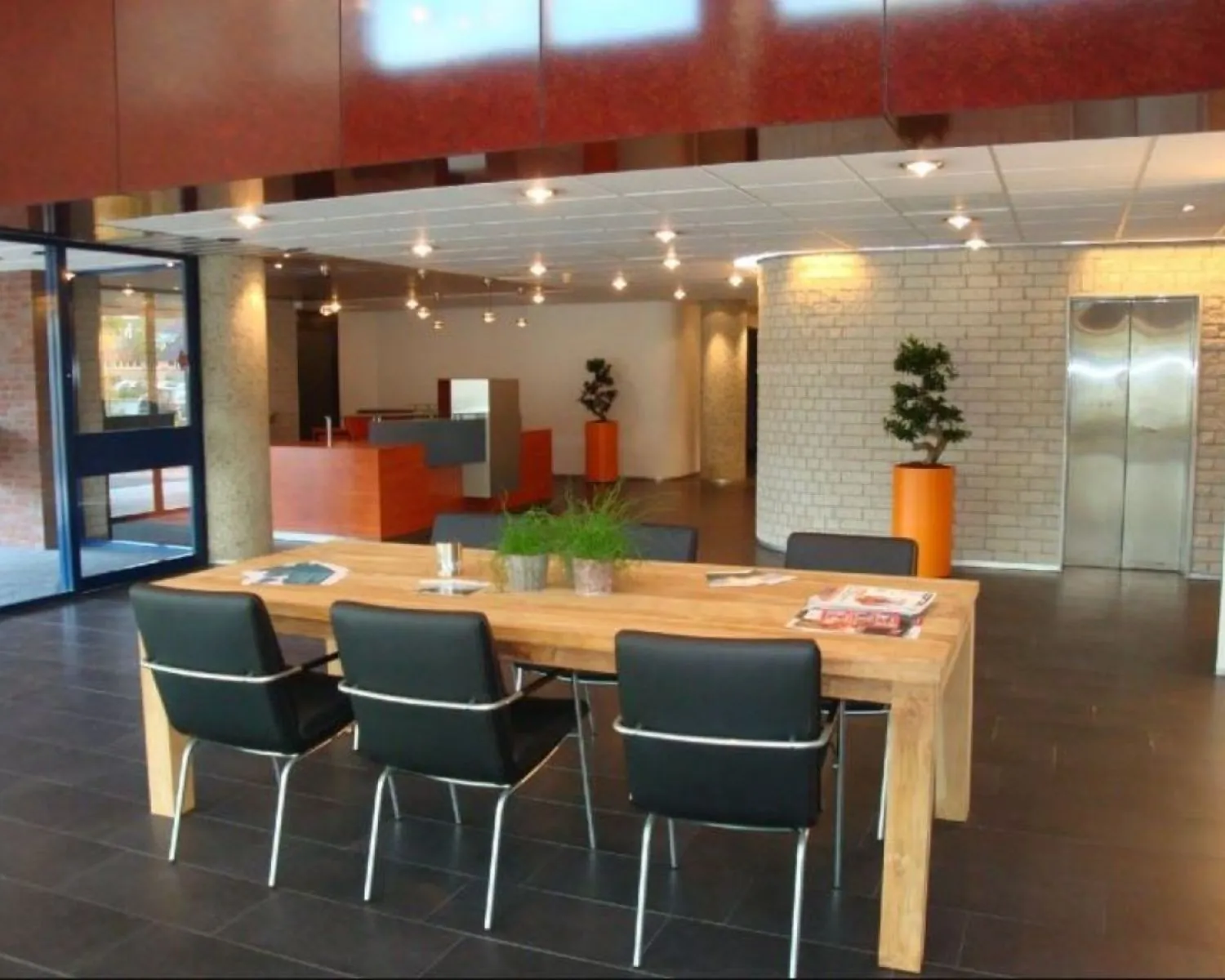 Moderne ontvangstruimte met houten tafel, zwarte stoelen en een lift in een kantoorgebouw aan de 's-Gravelandseweg 258.