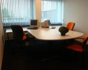 Kantoorruimte aan de 's-Gravelandseweg 258 met bureau, drie oranje stoelen, twee oude computerschermen en een plant.