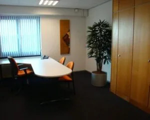 Moderne kantoorruimte met vergadertafel, oranje stoelen, plantenbak en ingebouwde houten kasten aan de 's-Gravelandseweg 258.