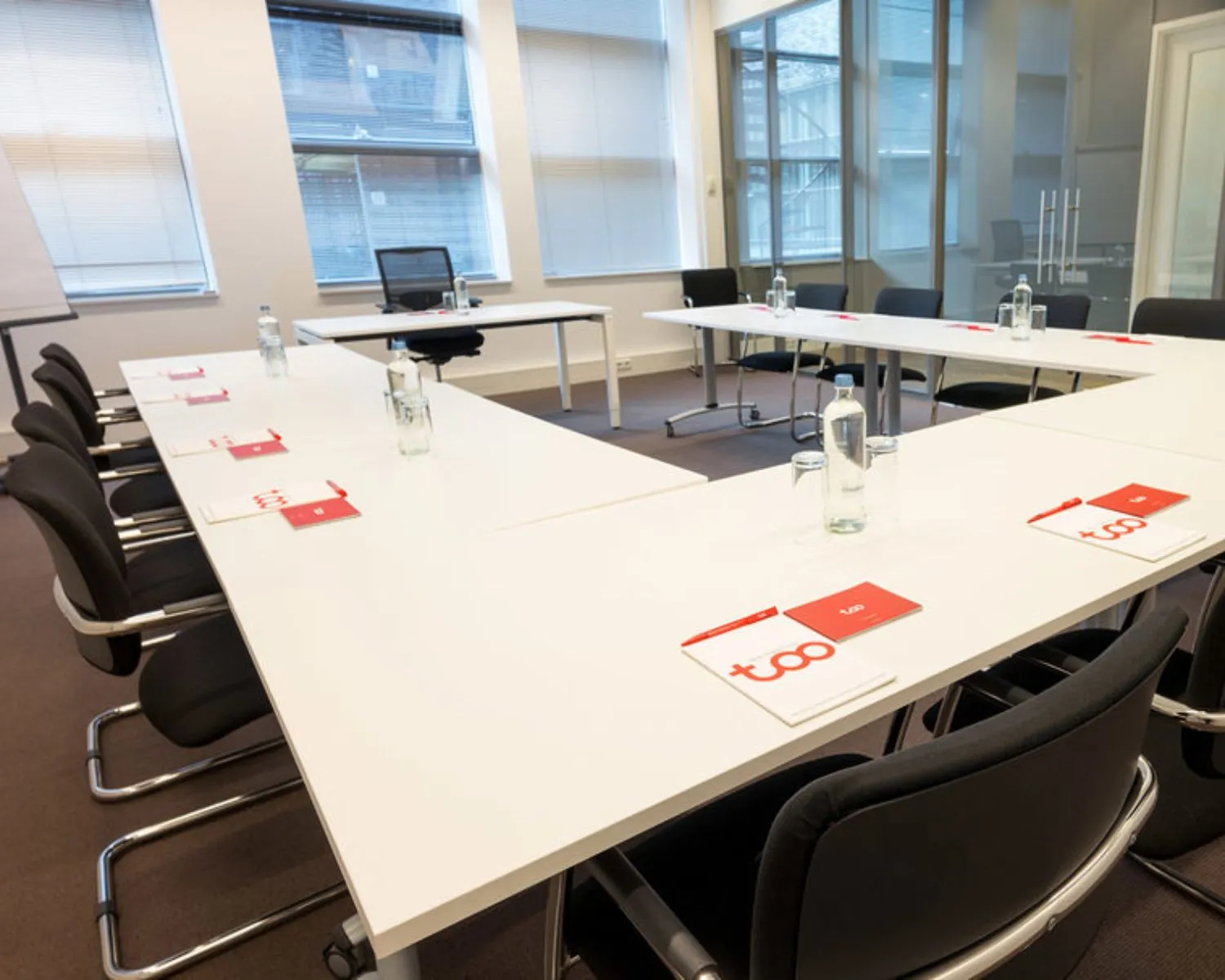 Vergaderruimte met U-vormige opstelling, zwarte stoelen, en notitieblokken in kantoor aan Smallepad 32 in Amersfoort.