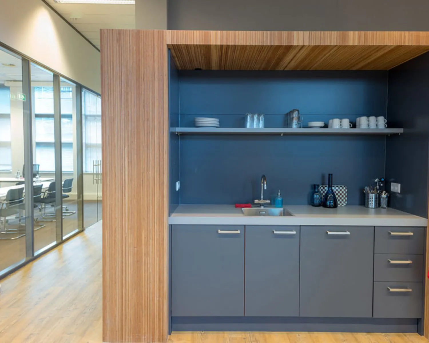Moderne kantoorpantry met grijze kasten, houten omlijsting en zicht op vergaderruimte aan het Smallepad 32 in Amersfoort.
