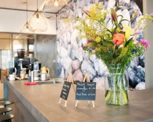 Modern koffiehoekje in een kantoorruimte aan het Smallepad 32 in Amersfoort, met bloemenvaas en menubordjes op de balie.