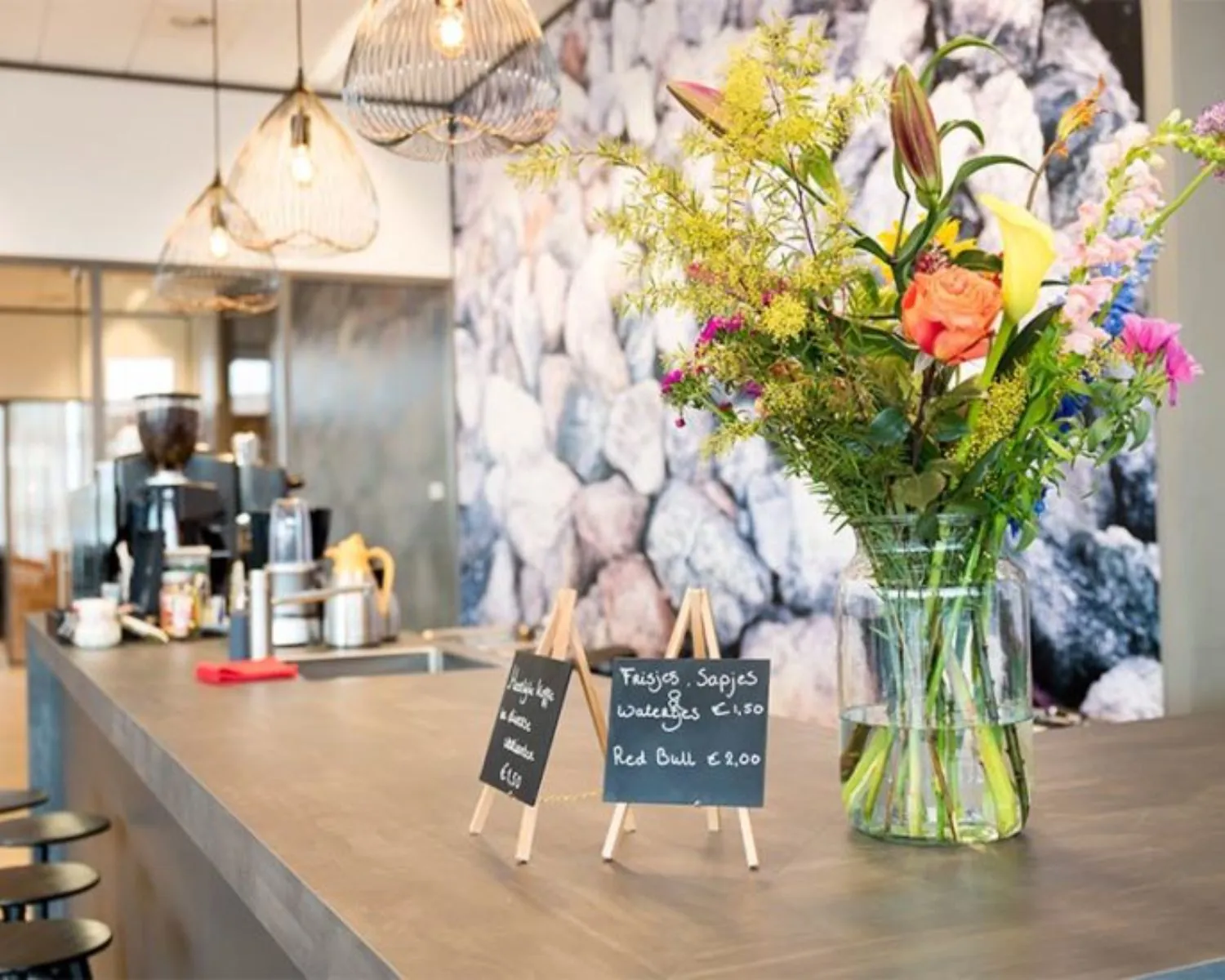 Modern koffiehoekje in een kantoorruimte aan het Smallepad 32 in Amersfoort, met bloemenvaas en menubordjes op de balie.