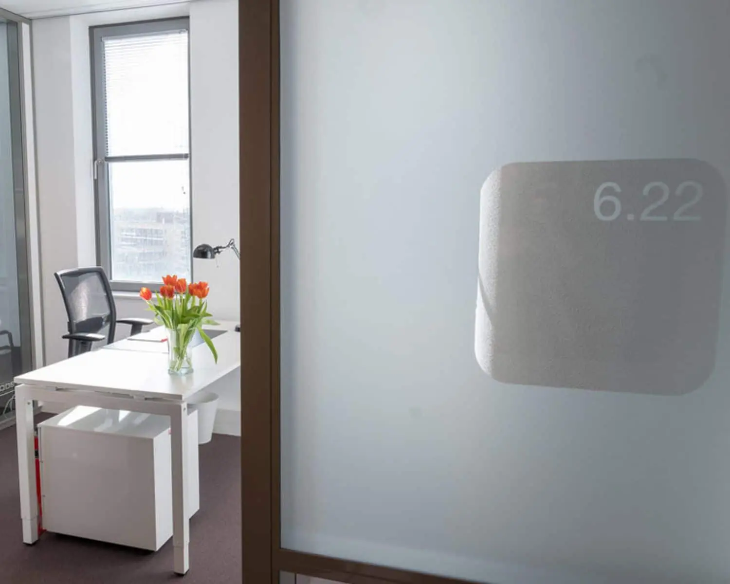 Moderne kantoorruimte met glazen deur, een wit bureau, bureaustoel en een vaas met oranje tulpen bij Smallepad 32 in Amersfoort.