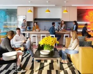 Moderne gemeenschappelijke kantoorruimte aan de Stadhouderskade 5 in Amsterdam met mensen die ontspannen en overleggen in een gezellige zithoek en bij een open keuken.