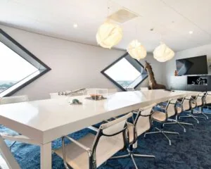 Moderne vergaderruimte in SugarCity Halfweg met lange witte tafel, designstoelen en grote ramen in diamantvorm.