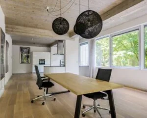 Moderne kantoorruimte met houten vloer, groot bureau, twee bureaustoelen en grote ramen met uitzicht op groen.