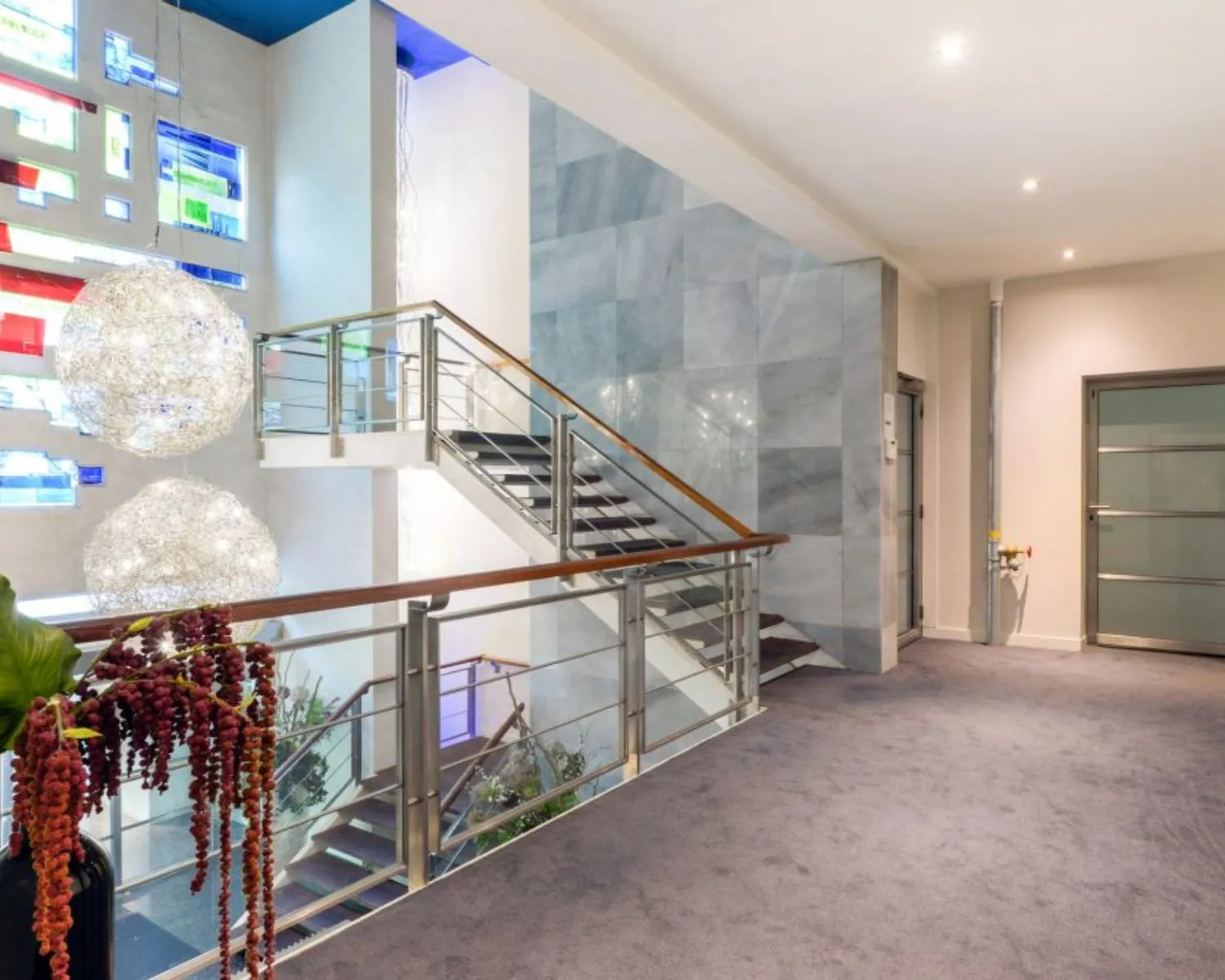 Moderne kantoorruimte met glazen trapleuning, kleurrijke wanddecoratie en opvallende hanglampen.