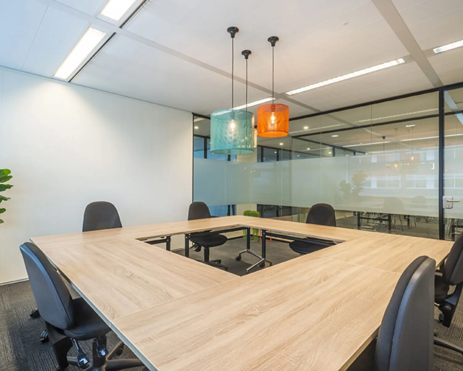 Moderne vergaderruimte in een kantoor aan de Tupolevlaan 41 in Schiphol met U-vormige tafel, zwarte stoelen en gekleurde hanglampen.