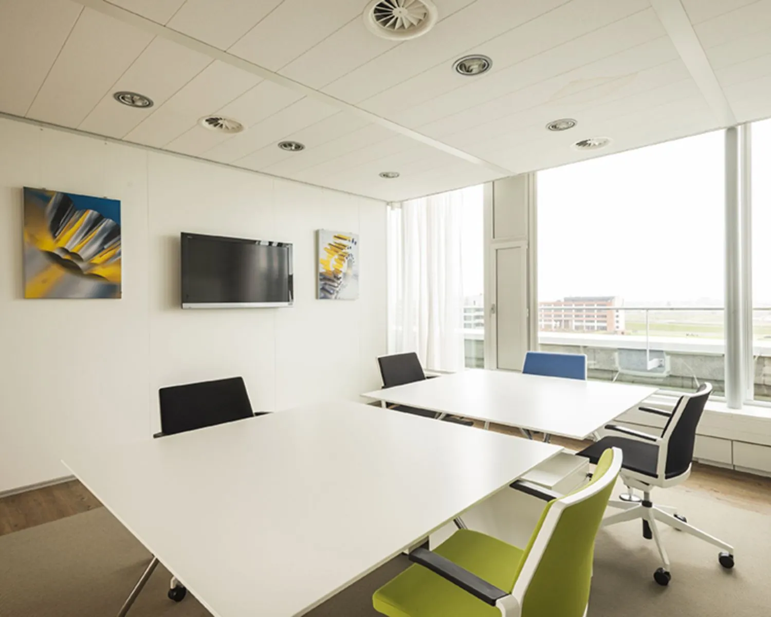 Moderne vergaderruimte met witte tafels, kleurige stoelen en groot raam in kantoor aan de Tupolevlaan 41 in Schiphol.