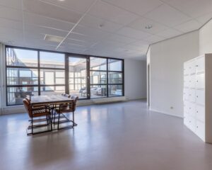Moderne, lichte kantoorruimte aan de Ukkelstraat 2 in Eindhoven met vergadertafel, grote ramen en witte lockerkasten.