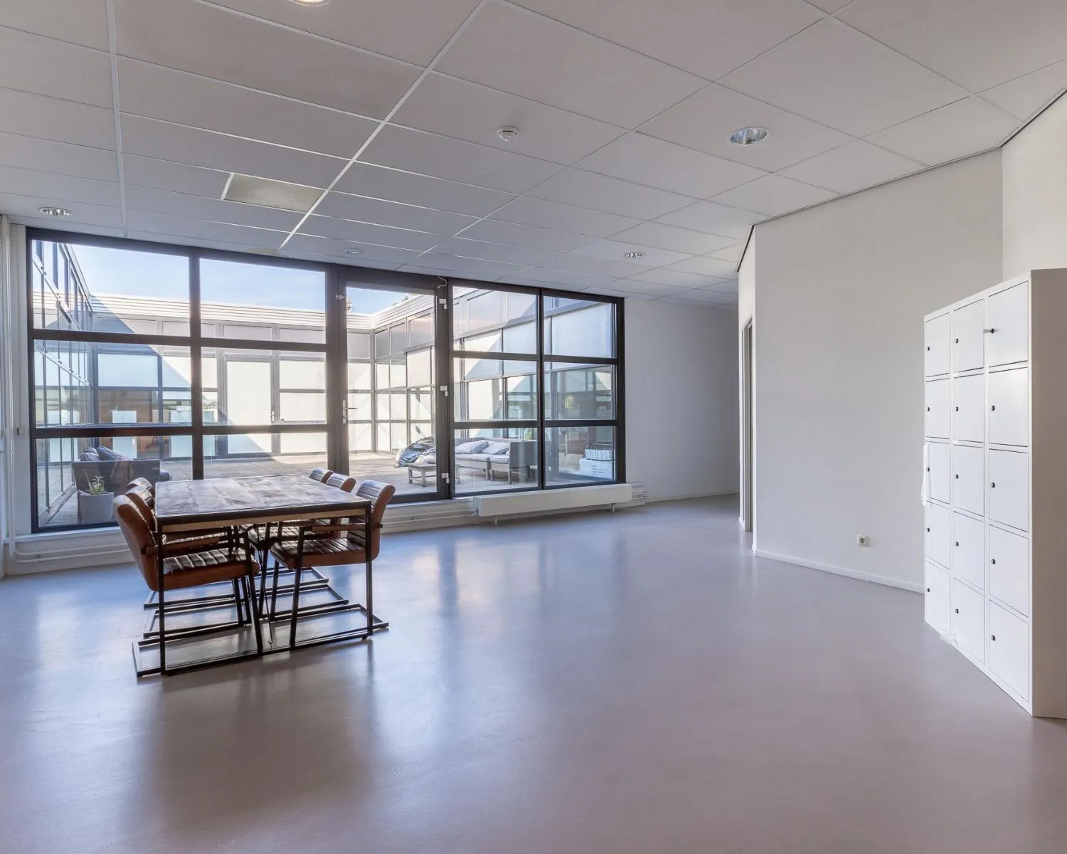 Moderne, lichte kantoorruimte aan de Ukkelstraat 2 in Eindhoven met vergadertafel, grote ramen en witte lockerkasten.