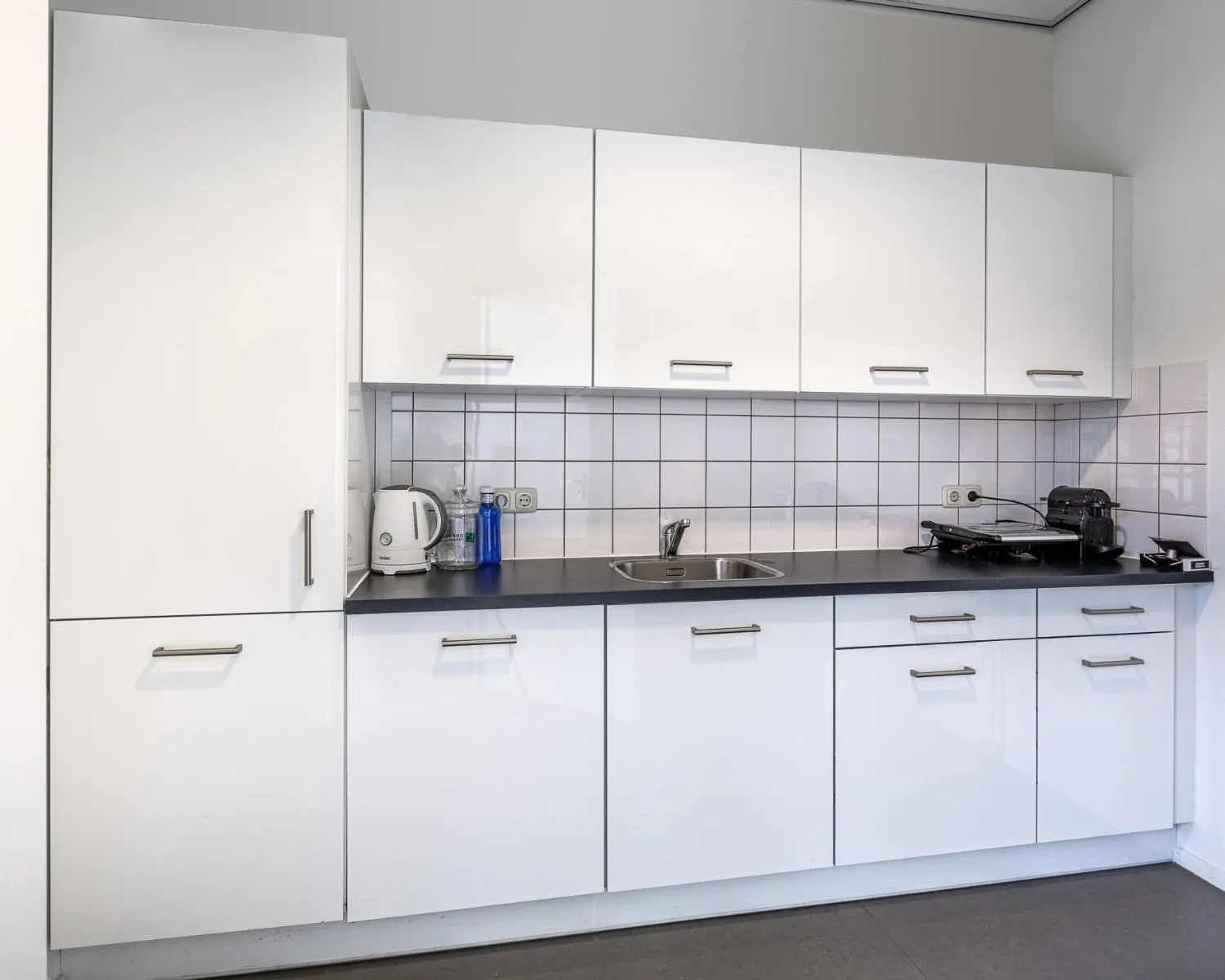 Moderne kantoorpantry met witte keukenkastjes, een spoelbak, waterkoker en koffiezetapparaat aan de Ukkelstraat 2 in Eindhoven.