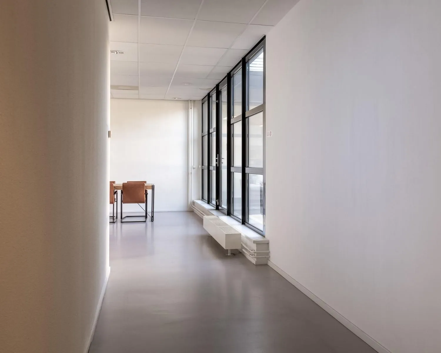 Lichte kantoorruimte in Eindhoven met glazen wand en modern bureau aan het einde van de gang.