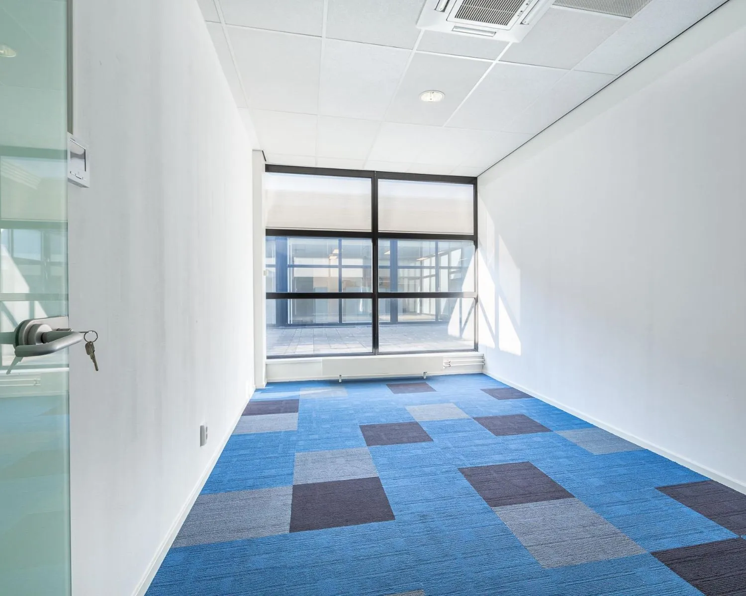 Lichte, lege kantoorruimte met blauw tapijt en grote raampartij aan de Ukkelstraat 2 in Eindhoven.