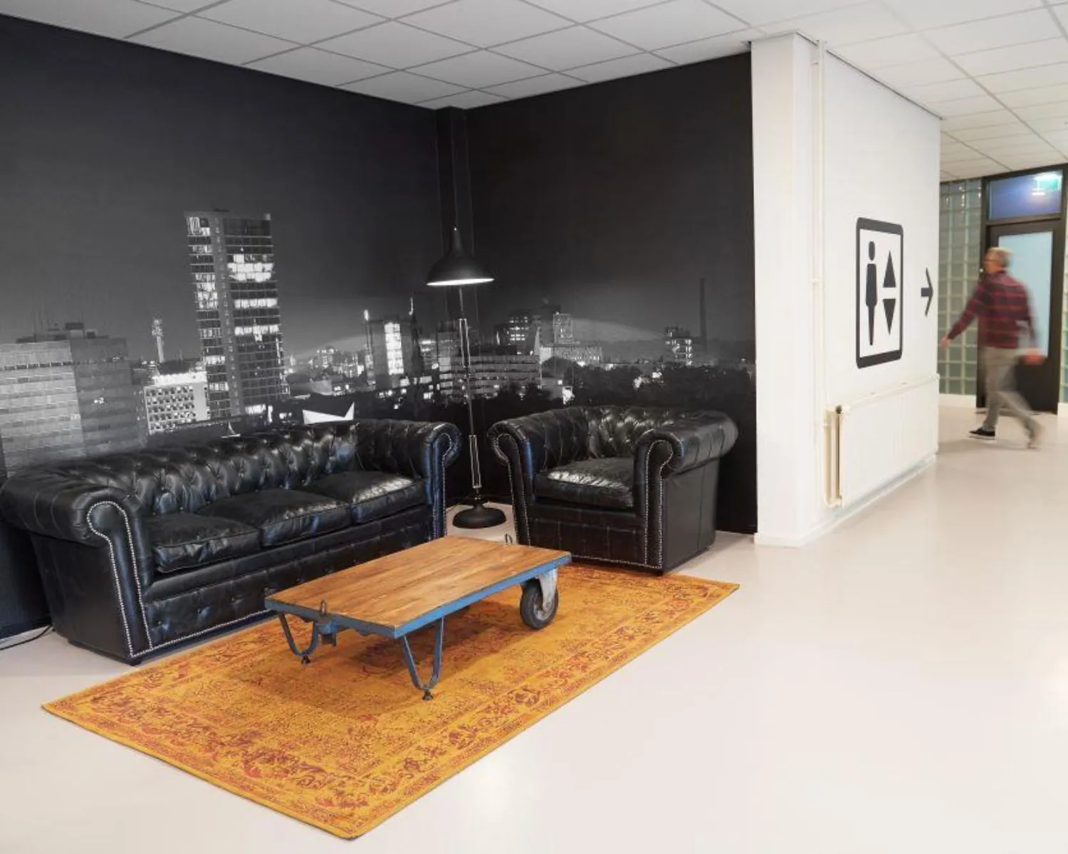 Moderne kantoorlounge met zwarte leren banken, een industriële salontafel en een stadsfoto op de muur aan de Ukkelstraat 2 in Eindhoven.