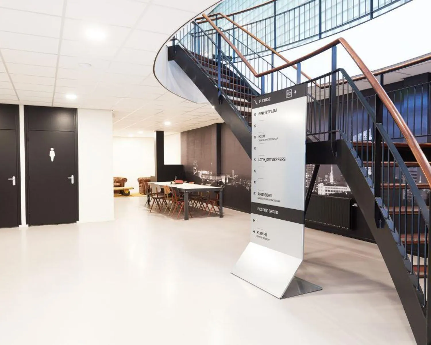 Moderne kantoorruimte in Eindhoven met trap, vergadertafel, wegwijzerbord en zwart-wit muurdecor.