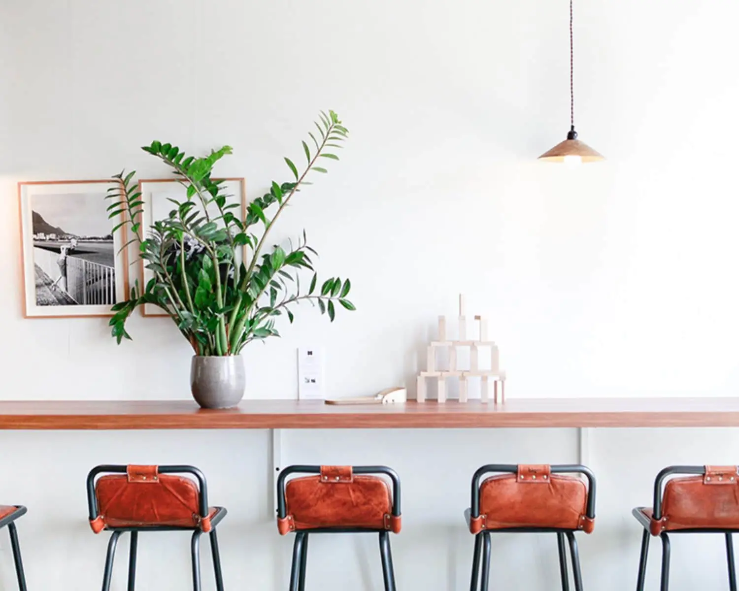 Moderne kantoorruimte aan de Wibautstraat in Amsterdam met hoge houten bar, leren barkrukken, een grote kamerplant en minimalistische decoratie.