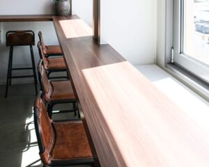 Lichte kantoorruimte aan de Wibautstraat in Amsterdam met hoge houten werktafel en leren barkrukken bij het raam.