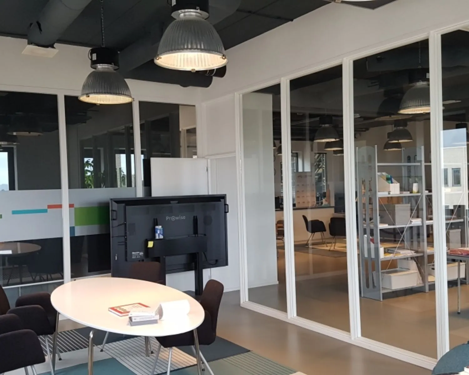 Moderne kantoorruimte met glazen wanden, vergadertafel en industriële plafondlampen aan de Zekeringstraat 17 in Amsterdam.