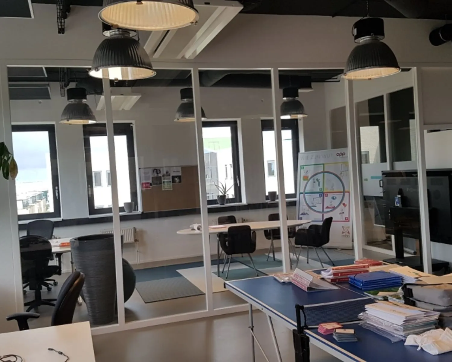 Moderne kantoorruimte in Amsterdam met glazen wanden, werkplekken en een tafeltennistafel gebruikt als werktafel.