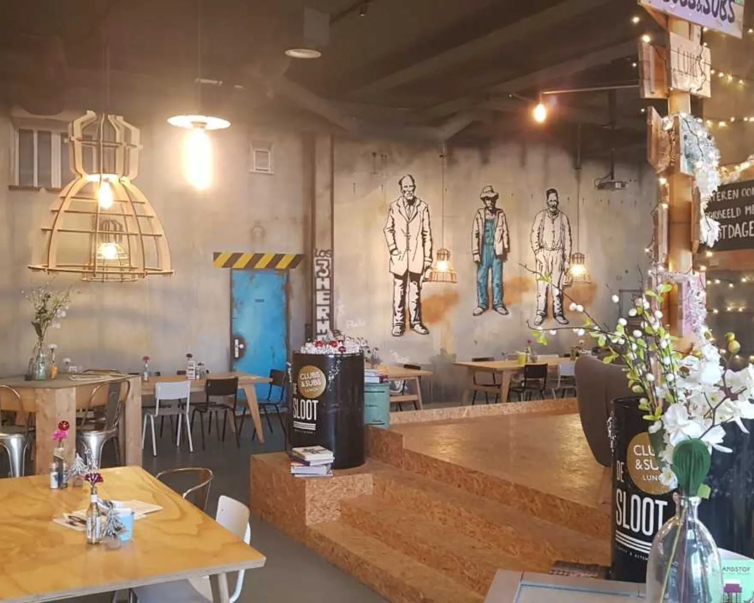 Industrieel ingerichte kantoorruimte met houten meubels, kunstmuur en decoratieve verlichting aan de Zekeringstraat 17 in Amsterdam.