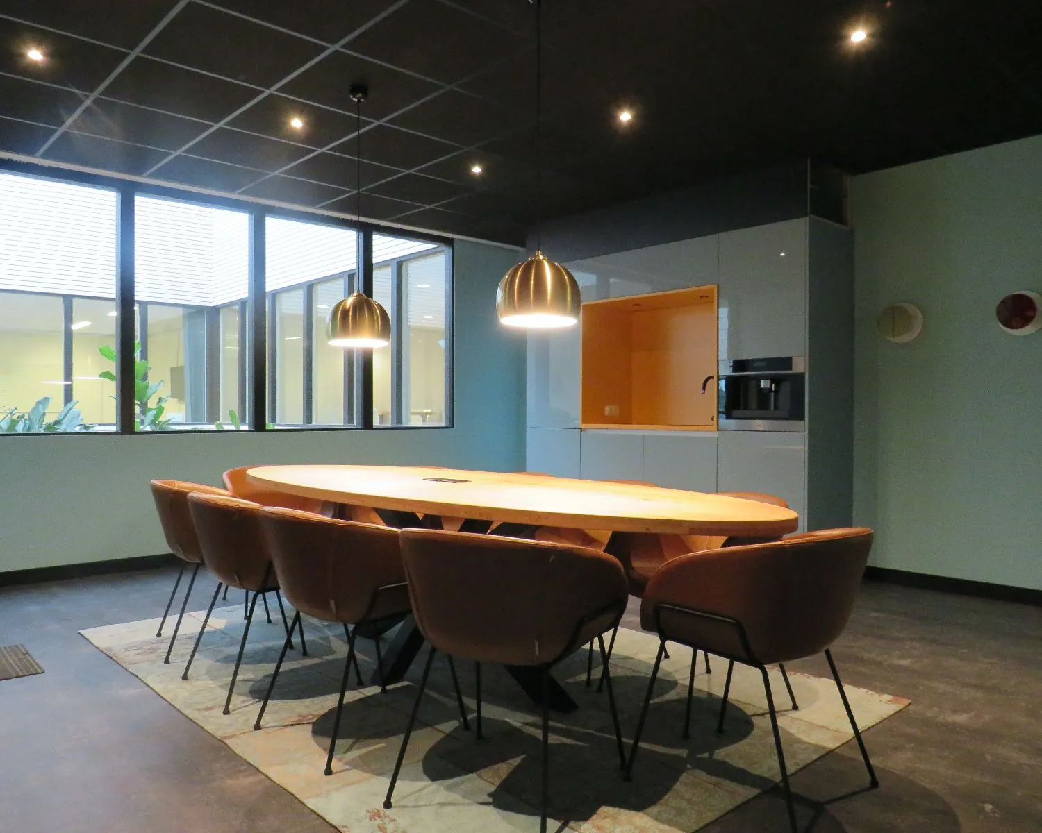 Moderne vergaderruimte met ovale houten tafel, acht stoelen en ingebouwde pantry in een kantoor aan de Zekeringstraat 43 in Amsterdam.