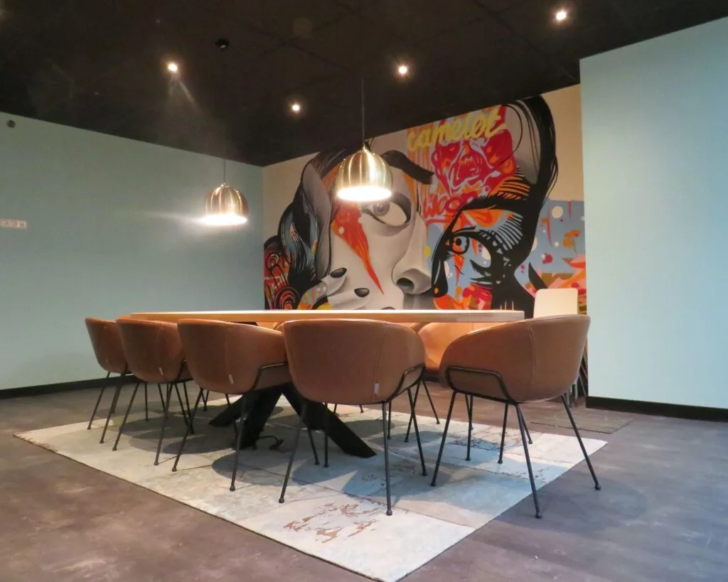 Moderne vergaderruimte met kunstzinnige muurschildering en leren stoelen aan een lange tafel in een kantoor aan de Zekeringstraat 43 in Amsterdam.