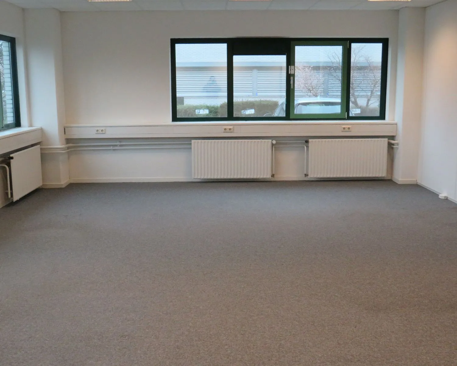 Leegstaand kantoor met grijze vloerbedekking en grote ramen aan de Zekeringstraat 43 in Amsterdam.