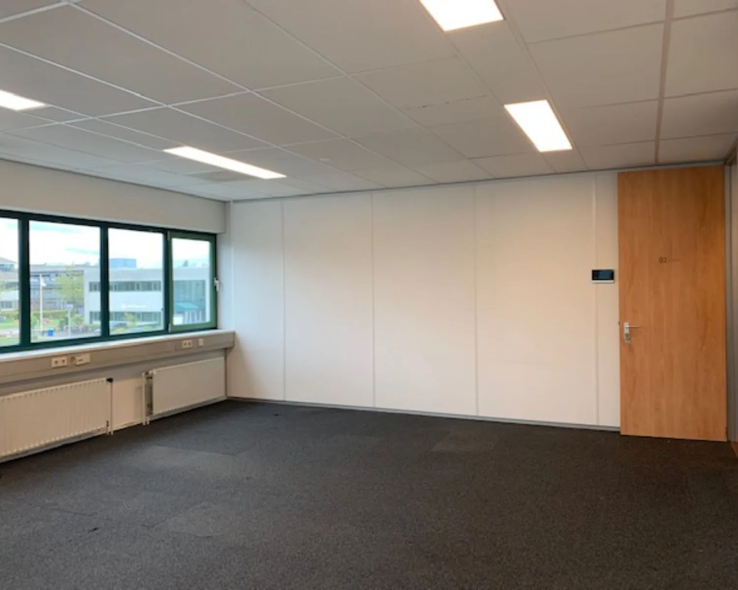 Lichte, lege kantoorruimte met tapijtvloer, systeemplafond, ramen en houten deur aan de Zekeringstraat 43 in Amsterdam.