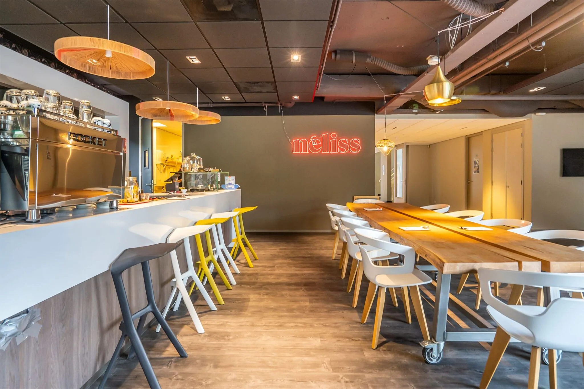 Moderne koffiebar en vergaderruimte bij Kanaalpark 140 met stijlvolle inrichting en een neon 'néliss'-bord aan de muur.