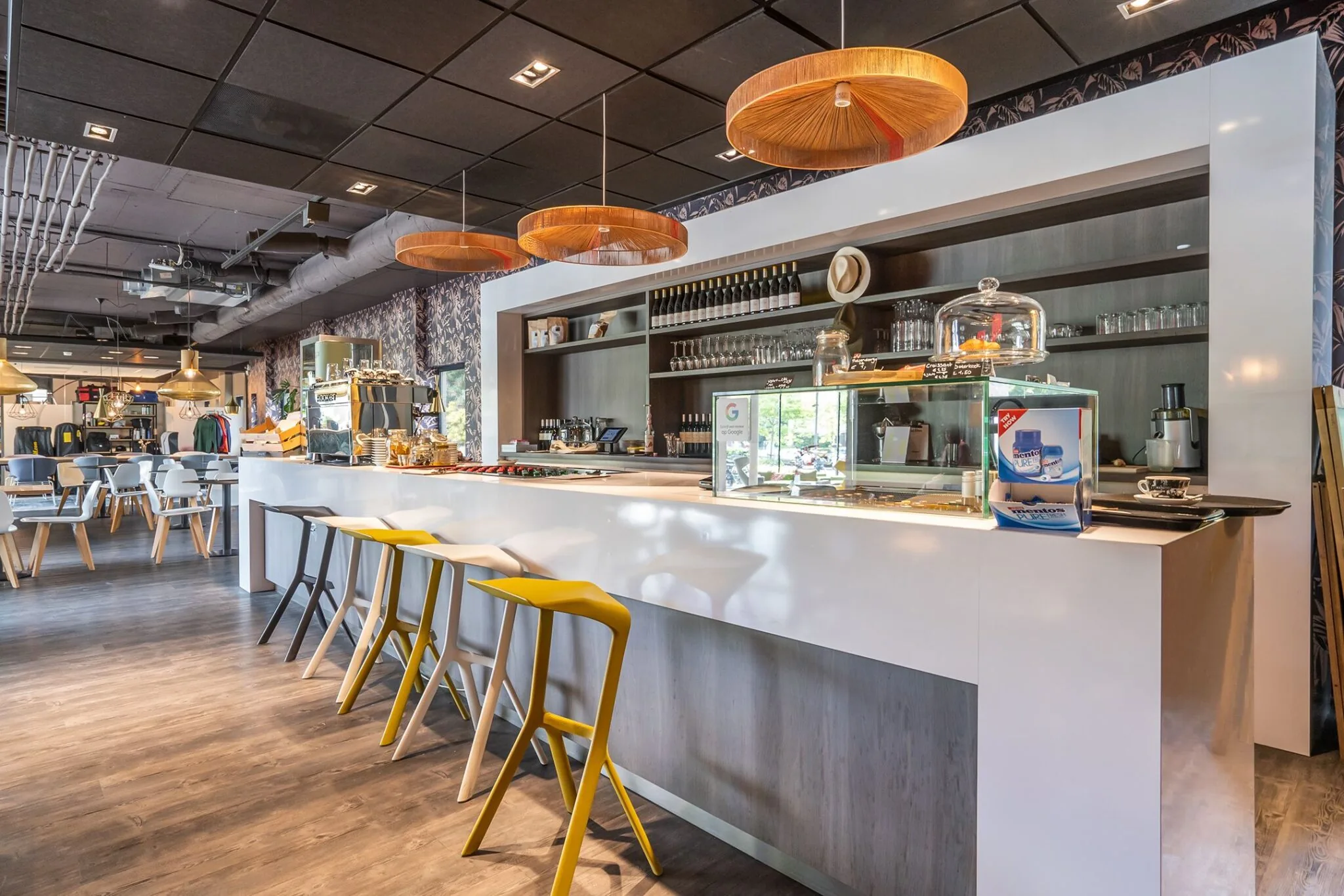 Moderne koffiebar met witte balie, kleurrijke barkrukken en warme hanglampen in Kanaalpark 140.