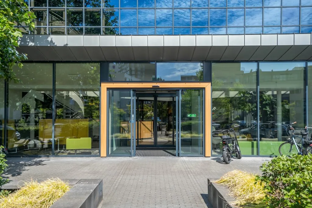Ingang van het moderne kantoorgebouw Kanaalpark 140 met glazen schuifdeuren en fietsen ervoor.