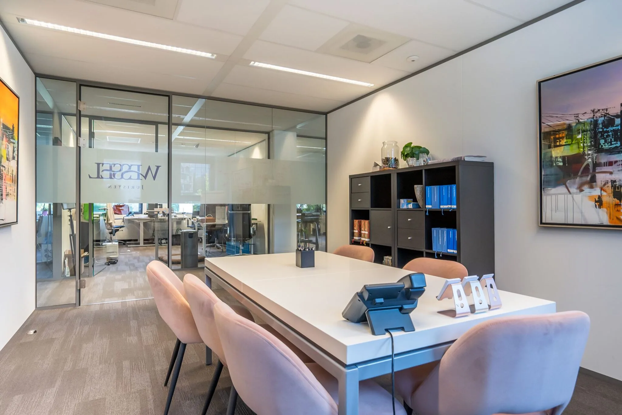 Moderne vergaderruimte in kantoor Kanaalpark 140 met glazen wanden, vergadertafel, roze stoelen en open kast.