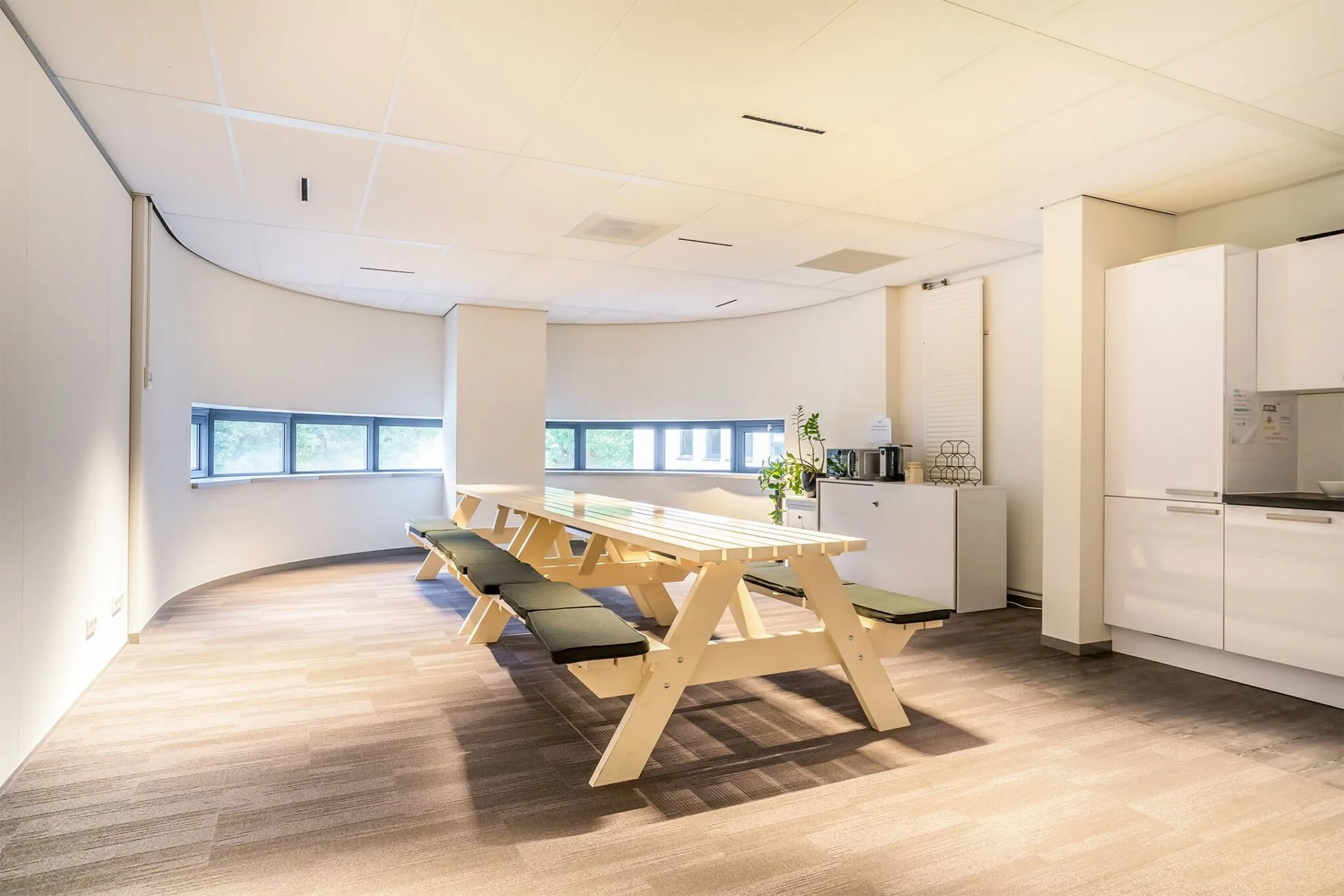 Moderne bedrijfskeuken met lange picknicktafels, zitkussens en een koffiemeubel bij Kanaalpark 140.