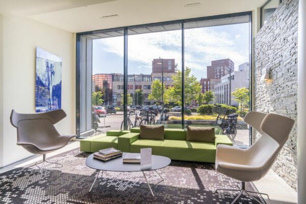 Moderne wachtruimte met groene bank, designstoelen en groot raam met uitzicht op Kanaalpark 140.