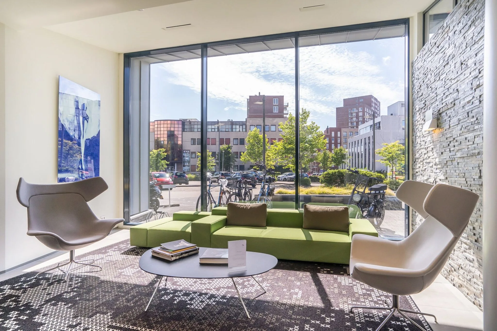 Moderne wachtruimte met groene bank, designstoelen en groot raam met uitzicht op Kanaalpark 140.