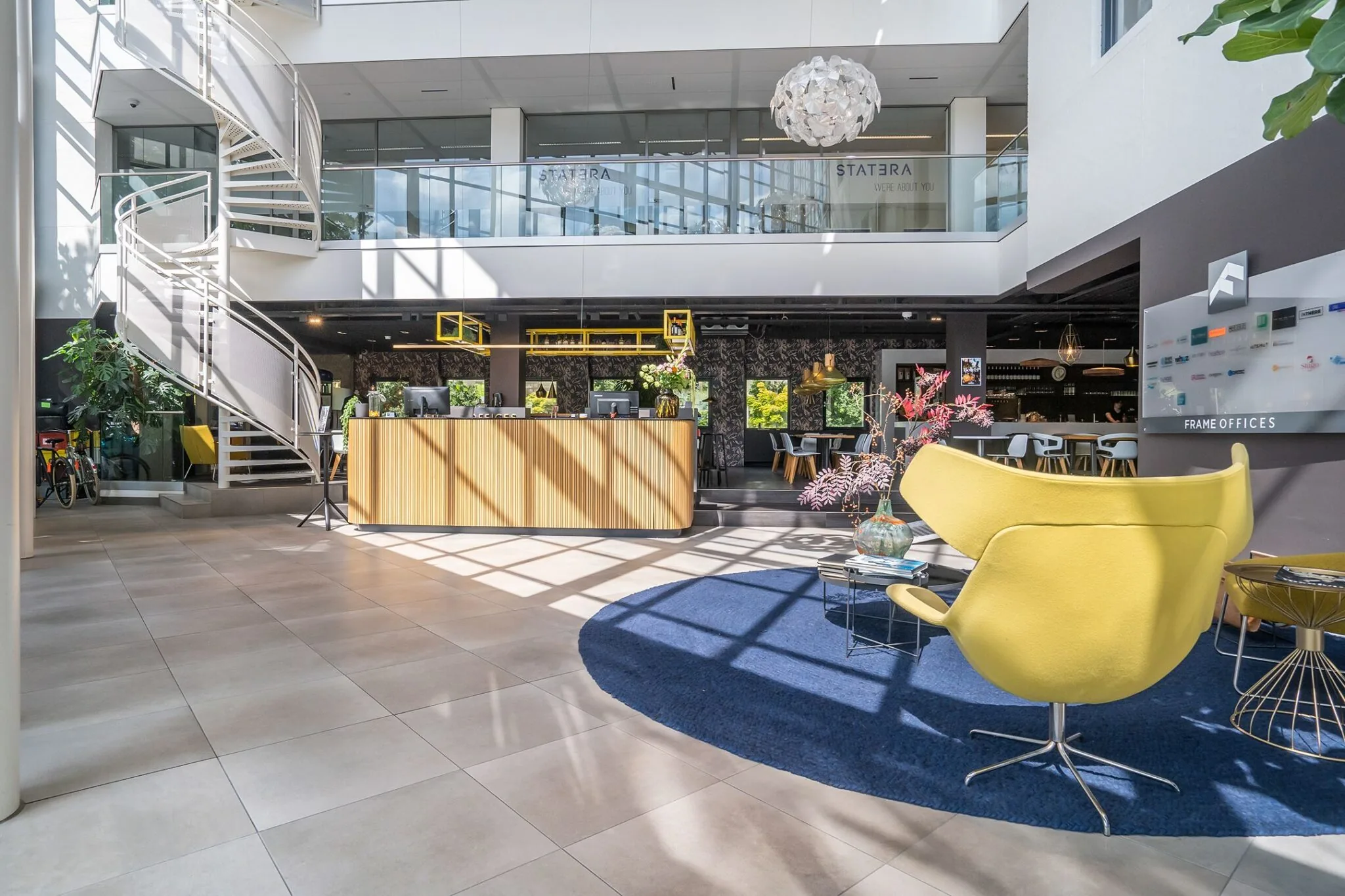 Moderne en lichte ontvangsthal van Kanaalpark 140 met designmeubilair, een houten balie en een opvallende wenteltrap.