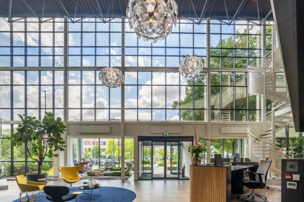Moderne en lichte entreehal van Kanaalpark 140 met hoge ramen, een ronde trap, designmeubels en een receptiebalie.