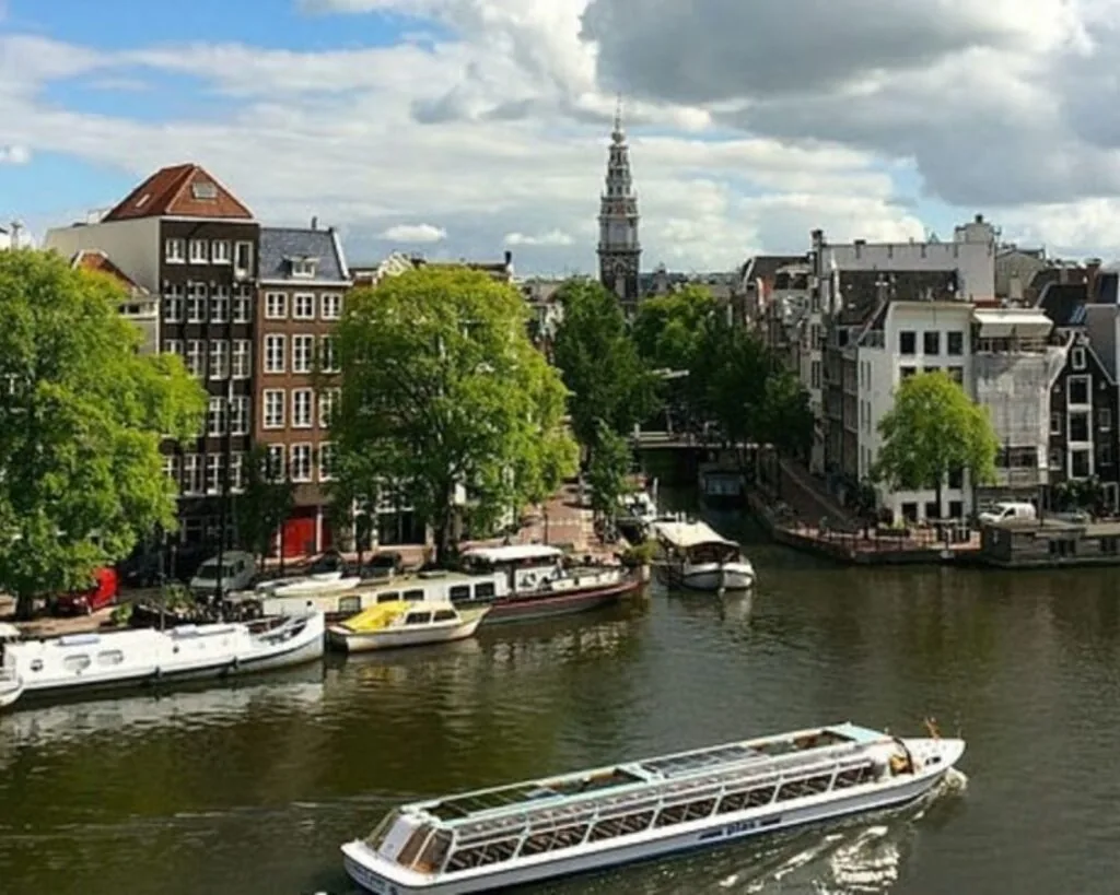 Uitzicht op de Amstel in Amsterdam met grachtenpanden, een rondvaartboot en de toren van de Zuiderkerk op de achtergrond.