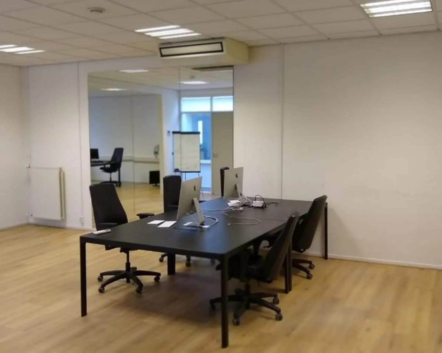 Moderne kantoorruimte aan de Amstel 62 in Amsterdam met bureau-opstelling, computers en draaistoelen op een houten vloer.