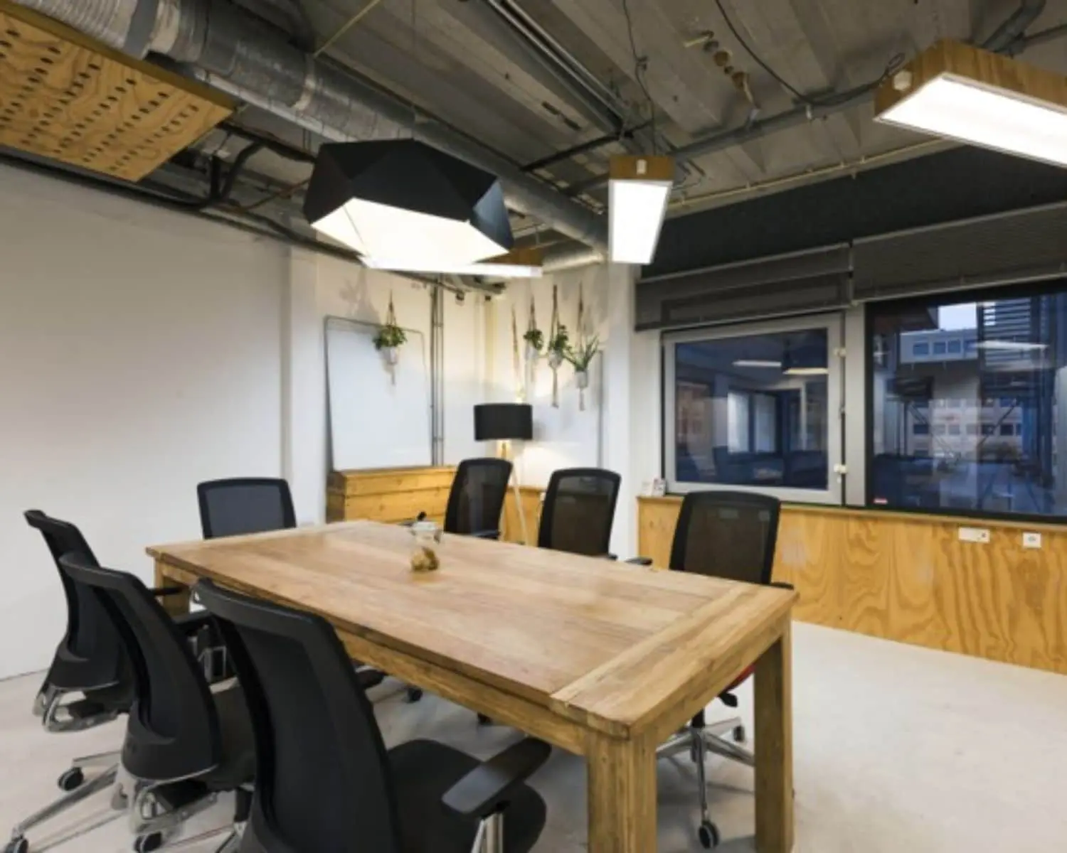 Vergaderruimte met houten tafel, zwarte bureaustoelen en industriële inrichting in een kantoor aan de Hogehilweg 20 in Amsterdam.