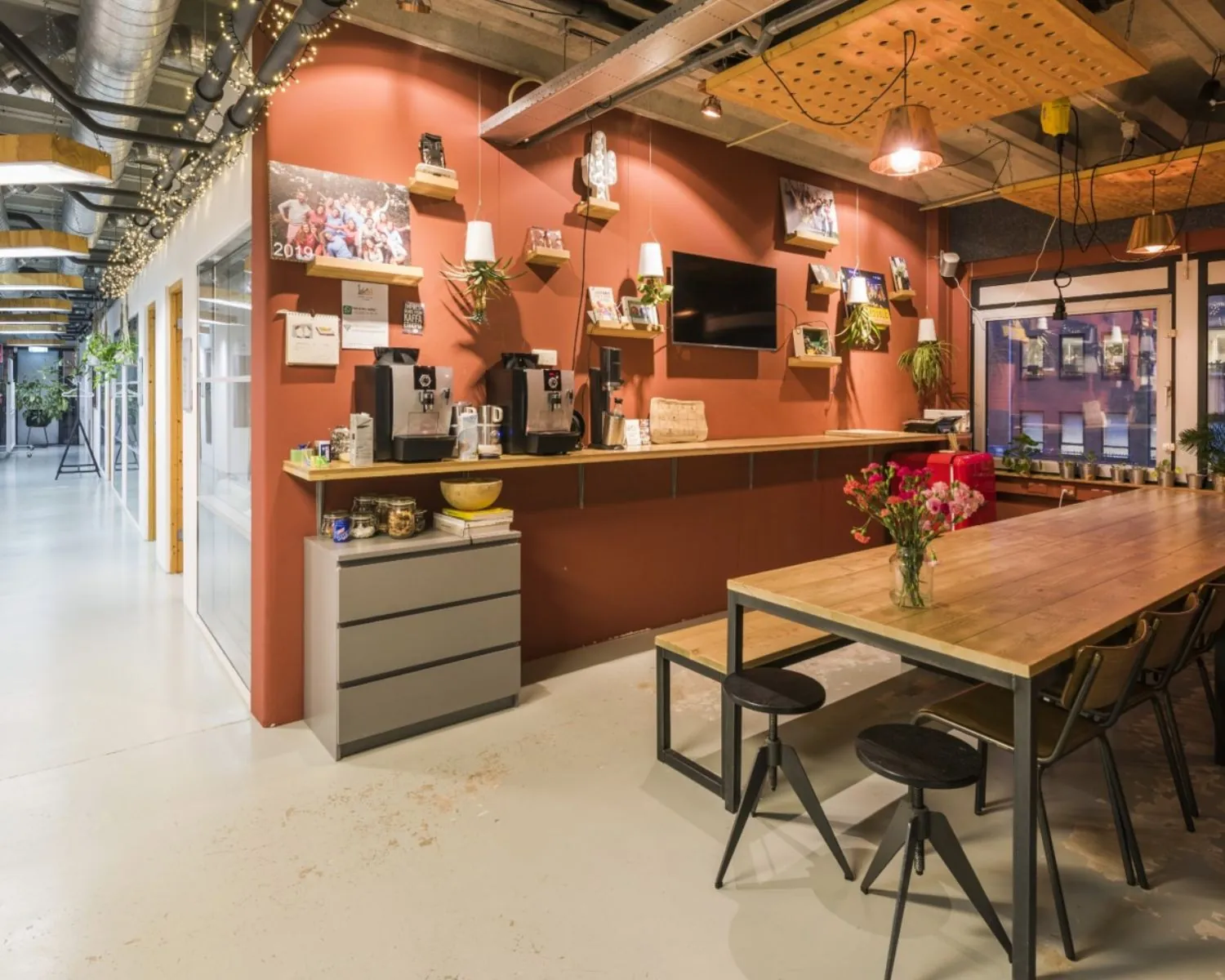 Moderne gemeenschappelijke kantoorruimte aan de Hogehilweg 20 in Amsterdam met koffiehoek, lange houten tafel en industriële inrichting.