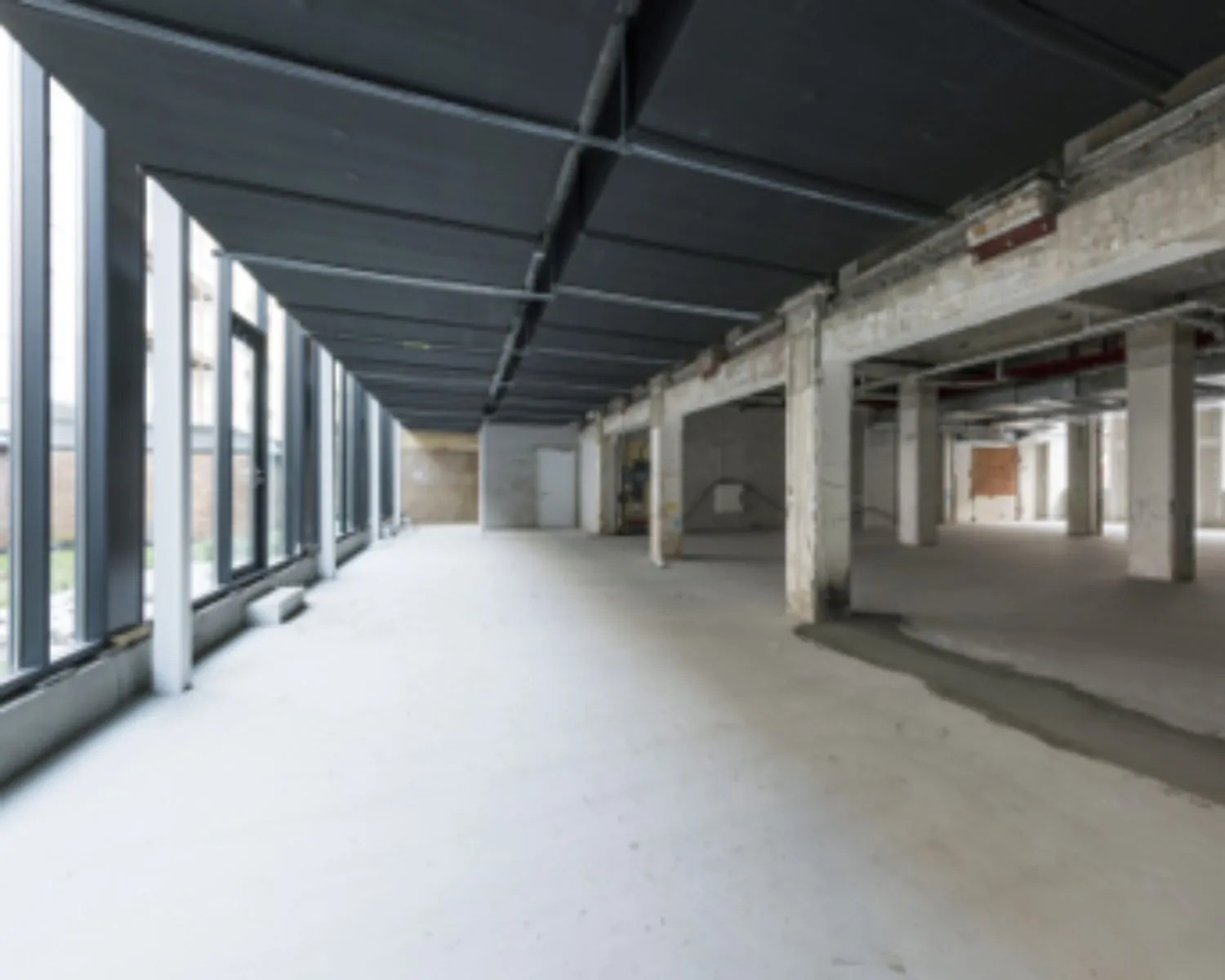 Leegstaande, industriële kantoorruimte aan de Karel du Jardinstraat 4 in Amsterdam met betonnen vloeren en grote ramen.