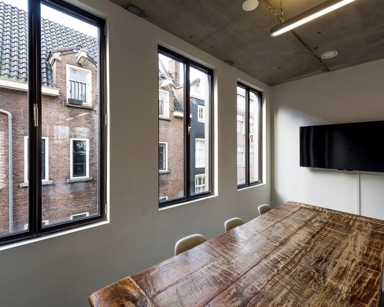 Vergaderruimte met houten tafel, grote ramen en uitzicht op traditionele panden aan de Bergstraat in Amsterdam.