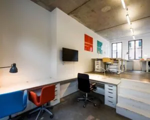 Moderne kantoorruimte aan de Bergstraat 6 in Amsterdam met meerdere bureaus, kleurrijke stoelen en industriële afwerking.