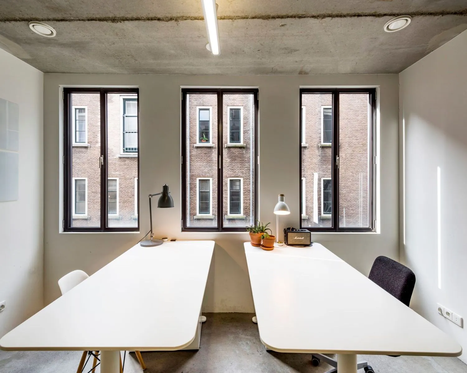 Moderne kantoorruimte aan de Bergstraat 6 in Amsterdam met twee bureaus, bureaulampen, planten en groot daglicht via ramen.