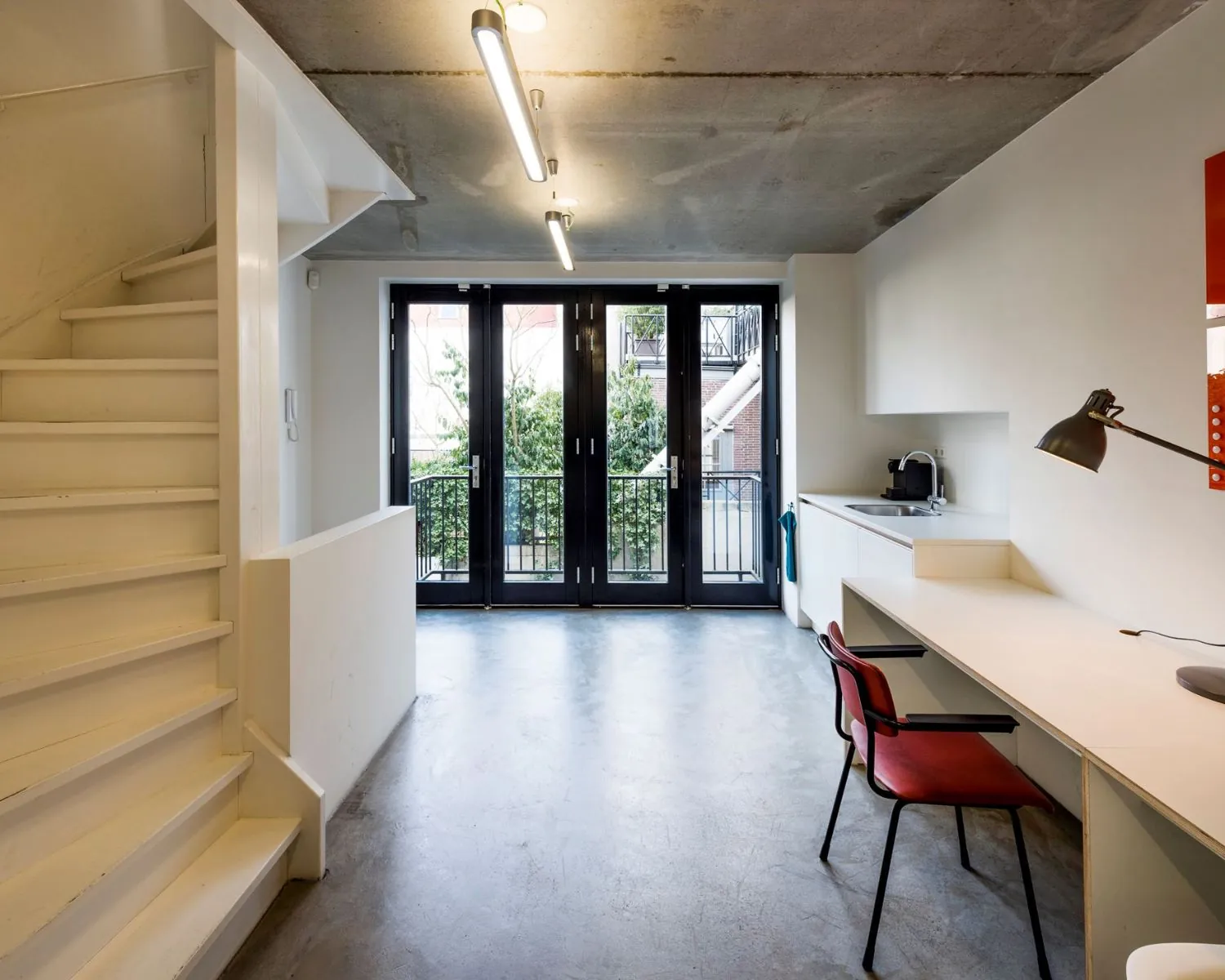 Moderne kantoorruimte aan de Bergstraat 6 in Amsterdam met werkplek, trap en openslaande deuren naar een balkon.